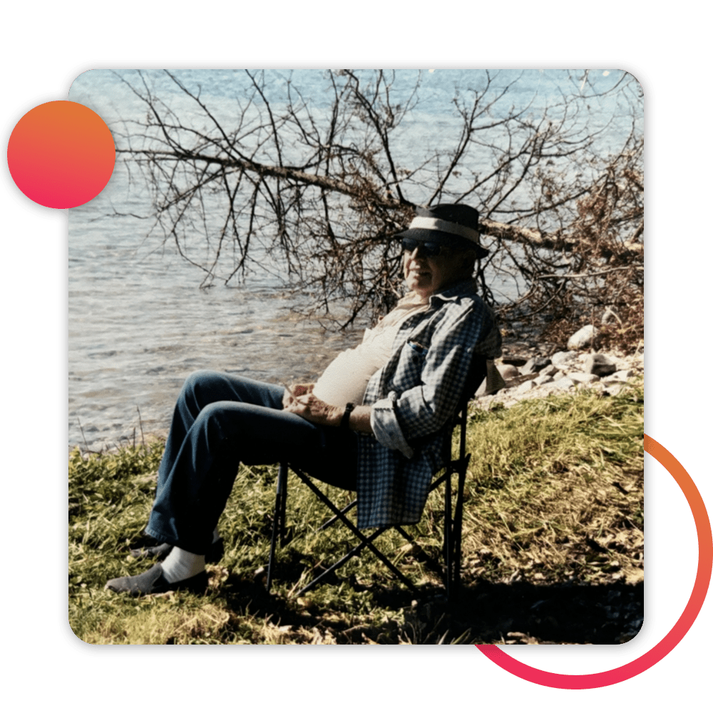 man in hat sitting lakeside, smiling at camera